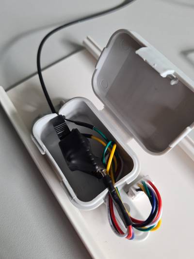 Nun ist die Abzweigdose geöffnet. In schwarzem Schrumpfschlauch versteckt ist ein RP2040-Zero-Board und eine TOSLINK-Buchse (3D-gedruckt). Ein USB-C-Stecker steckt im Board und geht in 4 Drähte über. Ein TOSLINK-Stecker steckt. Zusammen passt alles nur gerade so in die Box. Der harte Teil des lötbaren USB-C-Steckers steht etwas aus der Dose hervor.