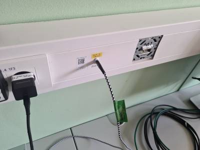 Ein Kabelkanal mit einer USB-C Buchse zwischen einer Steckdose und Ethernetdose. Die USB-C Buchse ist mit einem Wiki-to-Label-Tag versehen, und mit "AUDIO IN: USB/AUX" beschriftet. Ein schwarz-weisses Kabel ist eingesteckt.