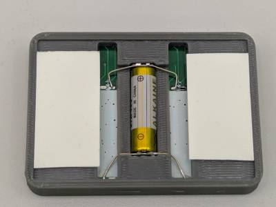 Rückseite mit eingebauter Batterie und angebrachten Klebestreifen. Rückseite mit eingebauter Batterie und angebrachten Klebestreifen.