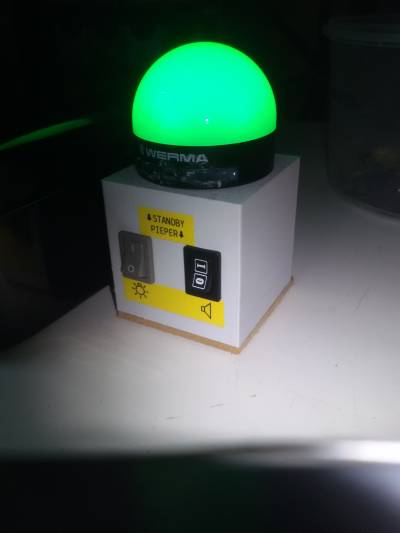 Eine Graue 3D-gedruckte Box mit 2 Schaltern und einer Leuchtkuppel (gerade grün). Die Schalter sind mit "Standby"/Lampensybol und "Pieper"/Lautsprechersymbol beschriftet. Eine Graue 3D-gedruckte Box mit 2 Schaltern und einer Leuchtkuppel (gerade grün). Die Schalter sind mit "Standby"/Lampensybol und "Pieper"/Lautsprechersymbol beschriftet.