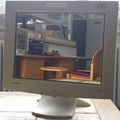 Bildschirm mit aufgeklebtem Spiegel im Fachschaftsraum, im Spiegel ist die Computerecke zu sehen, hinter dem Monitor ein Fenster mit Heizkörper darunter.
